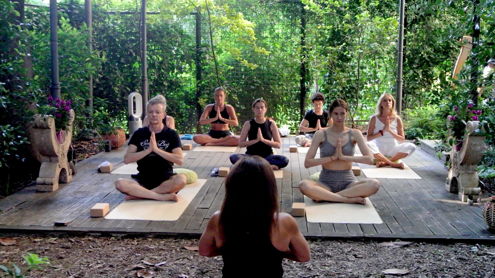 The full group seated with palms together in a closing gesture, harp visible in the background