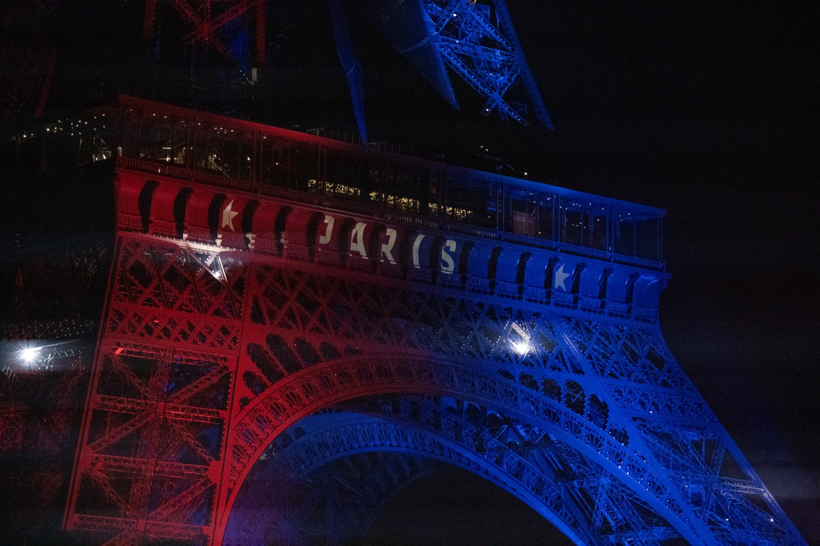 Close-up of the Eiffel Tower illuminated in red and blue with "PARIS" lit along its first level