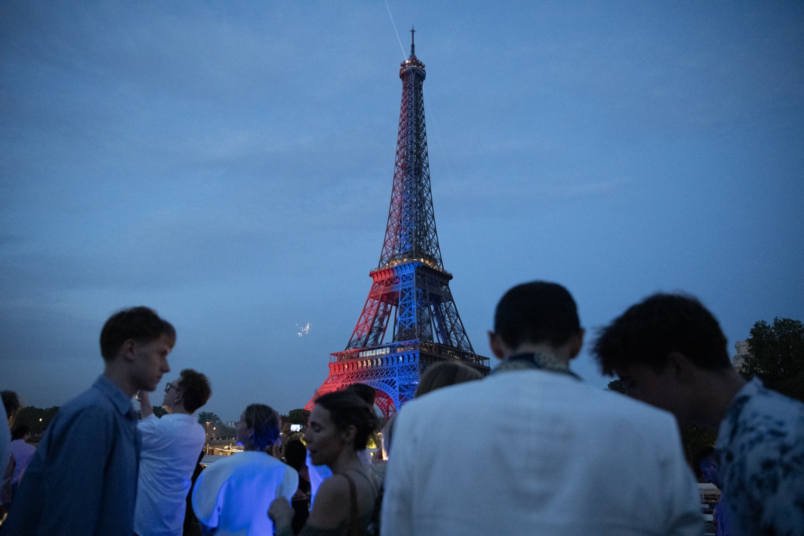 The Eiffel Tower illuminated in the French tricolour at dusk, seen from the Seine