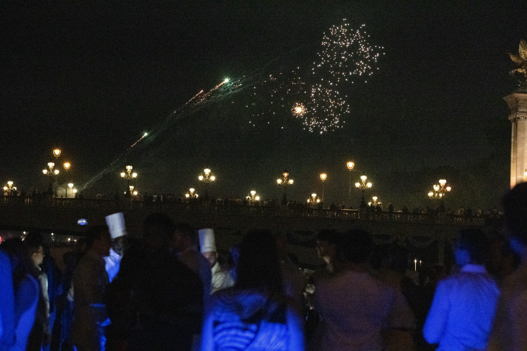 Fireworks bursting over Pont Alexandre III at night, guests watching from the yacht's deck